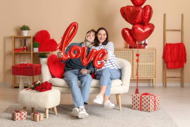 Young couple with air balloon in shape of word LOVE at home. Valentine's day celebration