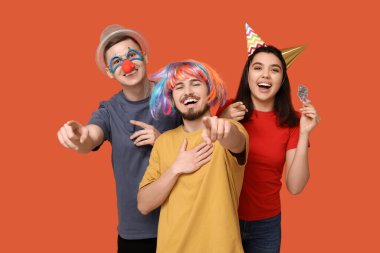 Tuhaf kılık değiştirmiş genç arkadaşlar. Turuncu arka plandaki izleyiciyi işaret eden kağıt balıklarıyla. 1 Nisan kutlamaları