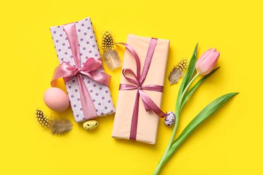 Lale çiçekli Paskalya yumurtaları, tüyler ve sarı arka planda hediye kutuları.