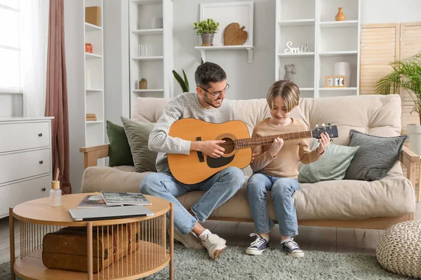 Private music teacher giving guitar lessons to little boy in living room