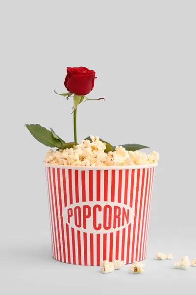 Bucket of popcorn with beautiful rose on blue background. Valentine\'s Day celebration
