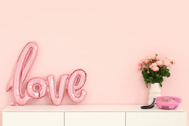 White cabinet with word LOVE made from balloons, bouquet of roses and vintage telephone near pink wall. Valentine's Day celebration