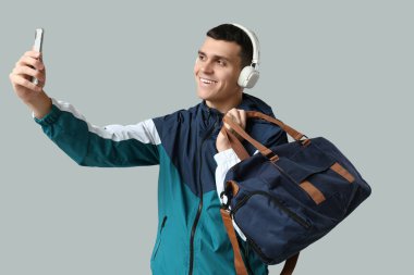 Spor çantalı genç adam gri arka planda selfie çekiyor.