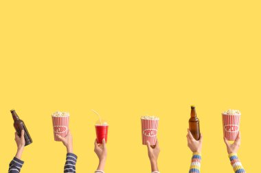 Sarı arka planda patlamış mısır ve bira kovaları olan bir sürü el.