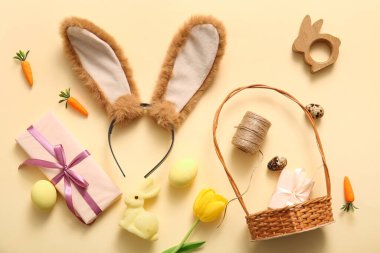 Tavşan kulaklı Paskalya kompozisyonu, bej arka planda boyanmış yumurta ve hasır sepet.
