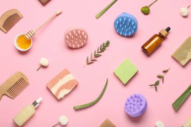 Saç derisi masaj aletleri, şampuan barları, kozmetik ürünleri şişeleri ve pembe arka planda çiçekler.