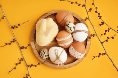 Paskalya yumurtalı ahşap tabak, tavşan figürü ve sarı arka planda dallar.