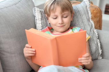 Kanepede uzanmış kitap okuyan sevimli küçük çocuk, yakın çekim.