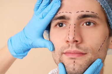 Plastik cerrah ve bej arka planda belirgin yüzü olan genç adam, yakın plan.