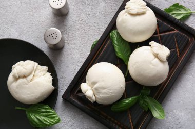 Ahşap tahta ve bir tabak lezzetli Burrata peyniri ve gri arka planda fesleğen.