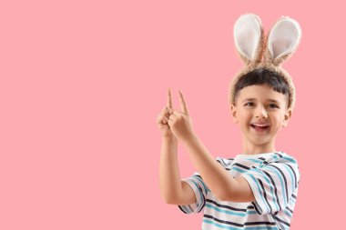 Tavşan kulağı takan şirin bir çocuk pembe arka plandaki bir şeyi işaret ediyor. Paskalya kutlaması