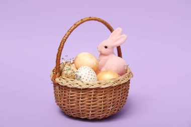 Paskalya yumurtaları ve leylak arkaplanda tavşan heykelciği olan sepet.