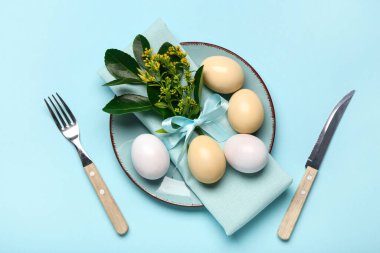 Mavi arka planda Paskalya yumurtaları, peçete ve çatal bıçak seti olan güzel bir masa.