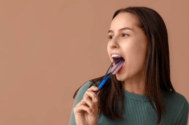 Kahverengi arka planda dil kazıyıcısı olan güzel genç bir kadın.