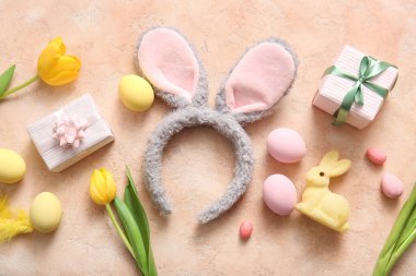 Paskalya yumurtalı tavşan kulakları, lale çiçekleri ve bej rengi grunge arka planda hediye kutuları.