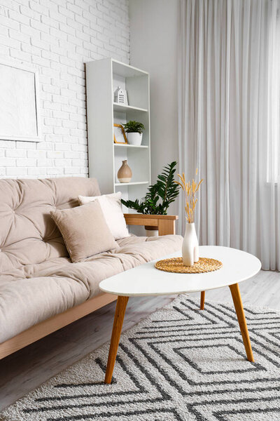 Interior of light living room with cozy sofa, houseplant and white coffee table