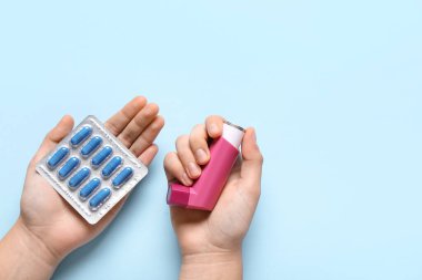 Astım spreyli çocuk elleri ve mavi arka planda haplar.