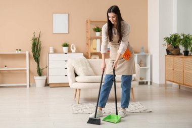 Genç kadın faraş ve süpürgeyle oturma odasını süpürüyor.