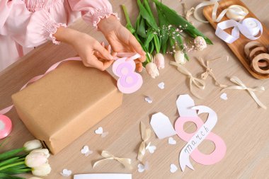 Arkaplanda Uluslararası Kadınlar Günü için hediye kutusu, paketleme malzemeleri ve lale çiçekleri olan bir kadın.