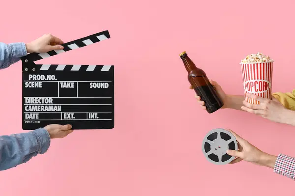 Hands with movie clapper, bucket of popcorn and beer on pink background