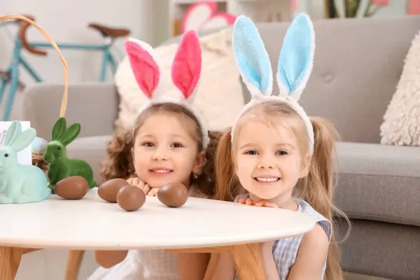 可爱的小女孩 长着小兔子耳朵 家里桌上放着巧克力复活节彩蛋 — 图库照片
