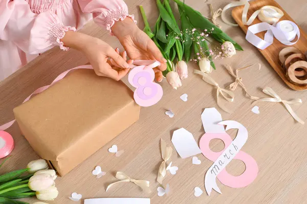 Arkaplanda Uluslararası Kadınlar Günü için hediye kutusu, paketleme malzemeleri ve lale çiçekleri olan bir kadın.