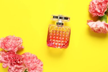 Sarı arka planda çiçekler olan pembe bir parfüm şişesi. Yakın çekim.