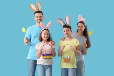 Mavi arka planda Paskalya yumurtaları olan tavşan kulaklı mutlu bir aile.