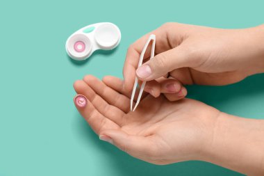 Cımbızlı kadın elleri ve turkuaz arka planda kontak lensli konteynır