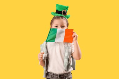 Sarı arka planda İrlanda bayrağı ve cüce şapkası olan şirin küçük bir kız. Aziz Patrick Günü kutlaması