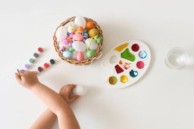 Küçük kız beyaz arka planda Paskalya için yumurta boyuyor.