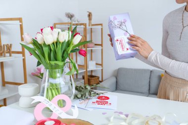 Hediye kutusu olan bir kadın, güzel lale çiçekleri ve ışıklı masada tebrik kartları. Uluslararası Kadınlar Günü
