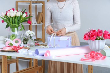 Uluslararası Kadınlar Günü için güzel çiçeklerle ışıklı masada hediye paketi hazırlayan kadın.