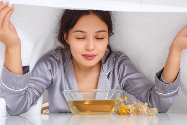 Genç Asyalı kadın mutfaktaki masada buhar solunumu yapıyor.