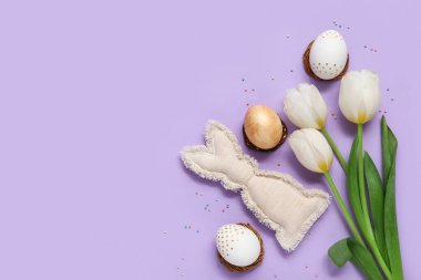 Paskalya yumurtaları ve mor arka planda oyuncak tavşanı olan güzel lale çiçekleri.