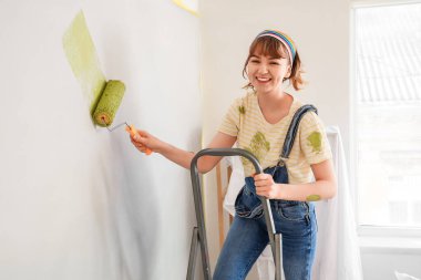 Odanın tamiri sırasında duvarı boyayan genç bir kadın.