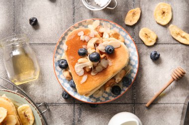 Kalp şeklinde lezzetli gözlemeler, kurumuş muz, yabanmersini ve bal içeren gri fayanslı bir tabak. Sevgililer Günü kutlaması