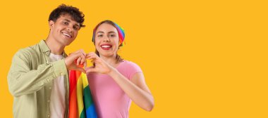 LGBT bayrağı taşıyan genç bir çift sarı arkaplanda kalp yapıyor ve metin için yer var.