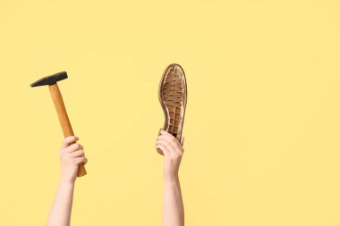 Ayakkabı tabanlı kadın eller ve sarı arka planda çekiç. Ayakkabı tamir konsepti