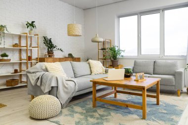 Rahat kanepeleri, çiçekleri, raf üniteleri ve dizüstü bilgisayarlı masası olan şık bir oturma odası.