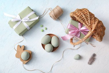 Hasır sepet ve hediye kutularında mavi grunge arka planda boyanmış Paskalya yumurtaları var.