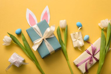 Hediye kutularıyla Paskalya yumurtaları, lale çiçekleri ve turuncu arka planda kağıt tavşan kulakları.