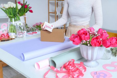 Hediye kutulu kadın, paketleme malzemeleri ve ışık masasında güzel lale çiçekleri. Uluslararası Kadınlar Günü