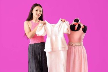 Mor arka planda manken ve kıyafetleri olan Asyalı bir kadın stilist.