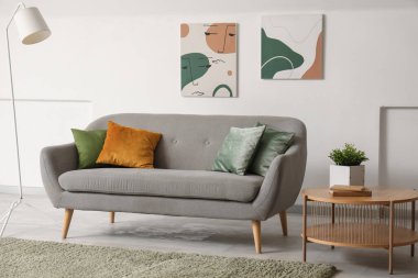 Aydınlık oturma odasının içinde şık bir kanepe, resimler ve masa var.