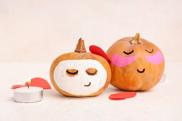 Pumpkin with drawn face, spa candle, paper hearts and clay mask on light background