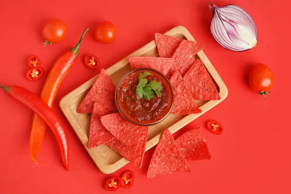 Wooden tray with red nachos, salsa sauce and chilli on color background