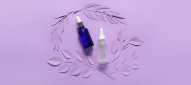 Eflatun arkaplanda kozmetik serumu ve kağıt yaprakları var. 