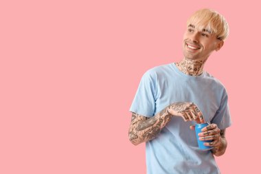 Dövmeli genç adam pembe arka planda bir kutu gazoz ile