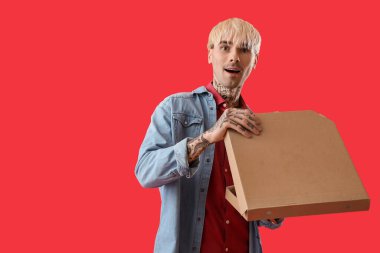 Kırmızı arka planda pizza kutusu olan sürpriz dövmeli genç adam.